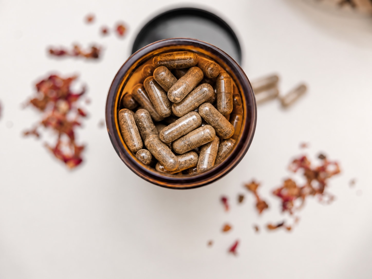 An amber jar of placenta capsules beside dried rose petals